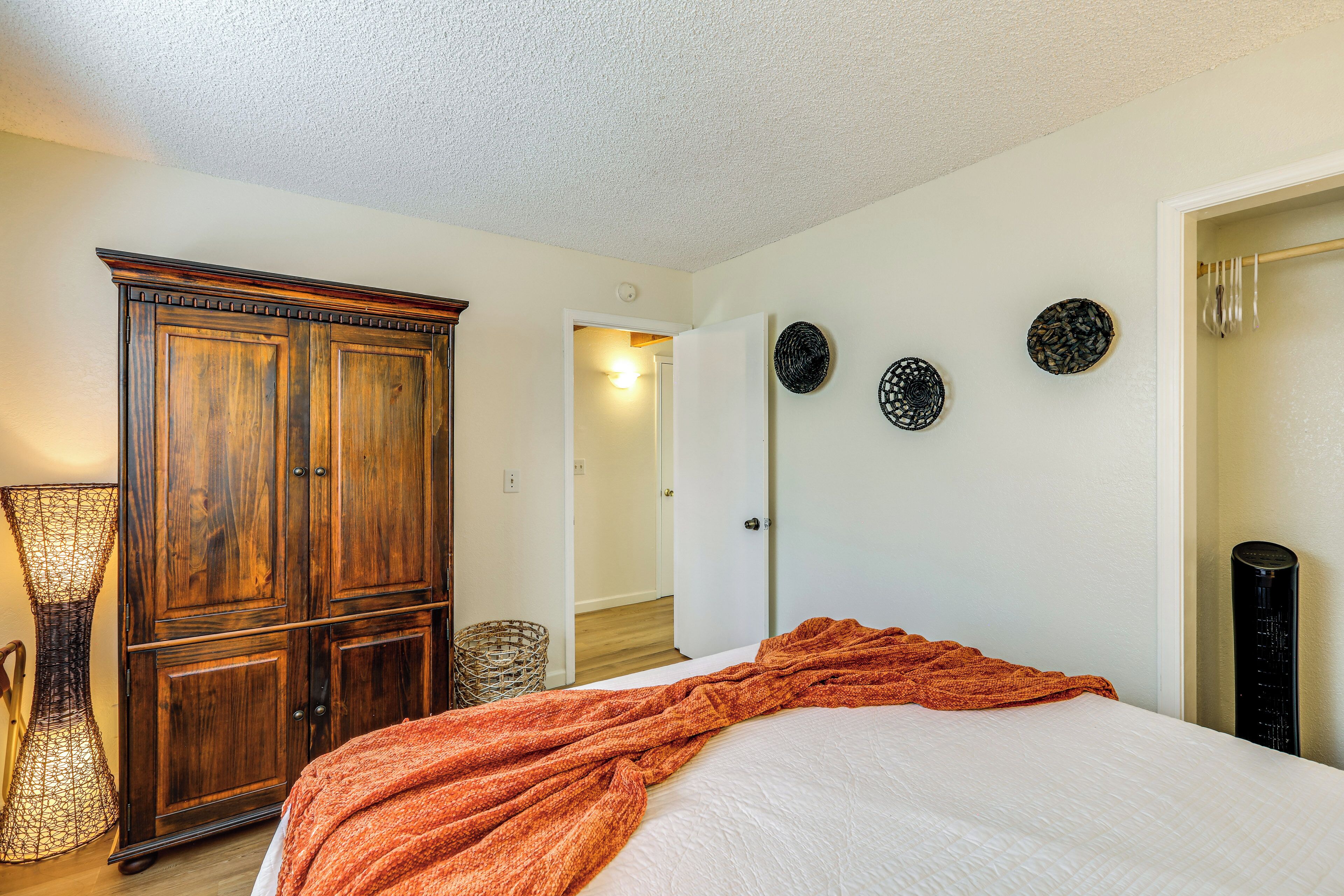 A bedroom with a large wooden wardrobe, a bed with an orange blanket, and three wall-mounted decorative plates.