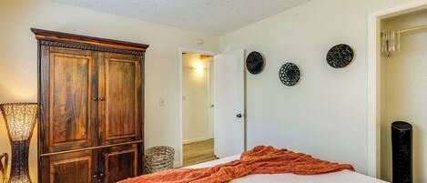 A bedroom with a large wooden wardrobe, a bed with an orange blanket, and three wall-mounted decorative plates.