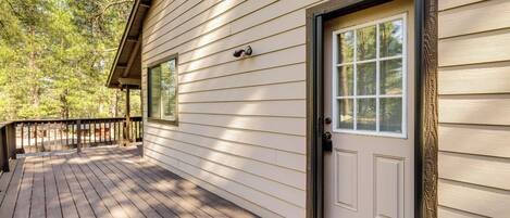 A wooden deck with a door and window, surrounded by trees.