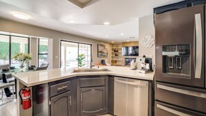 Una cucina moderna con frigorifero in acciaio inossidabile, forno integrato e lavastoviglie. È presente un'ampia finestra che offre luce naturale e vista sull'esterno.