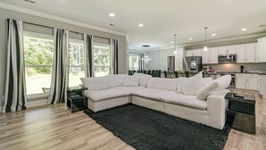 A modern living room with a sectional sofa, a black rug, and a kitchen area with white cabinets and a microwave. - Secluded 18-acre Retreat in Staley w/ Game Room (Staley)