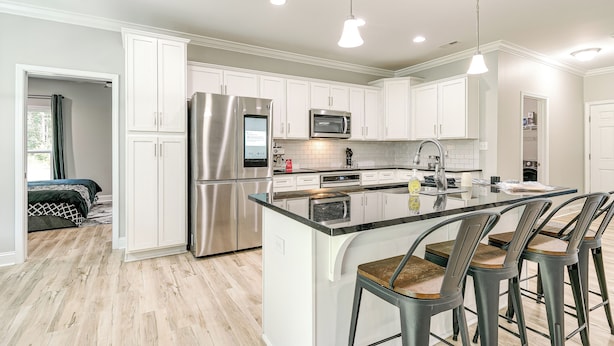 A modern kitchen with white cabinets, stainless steel appliances, and a central island with bar stools. - Secluded 18-acre Retreat in Staley w/ Game Room (Staley)