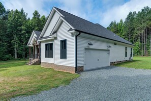 Une maison de plain-pied avec un garage, une véranda et une allée gravillonnée.