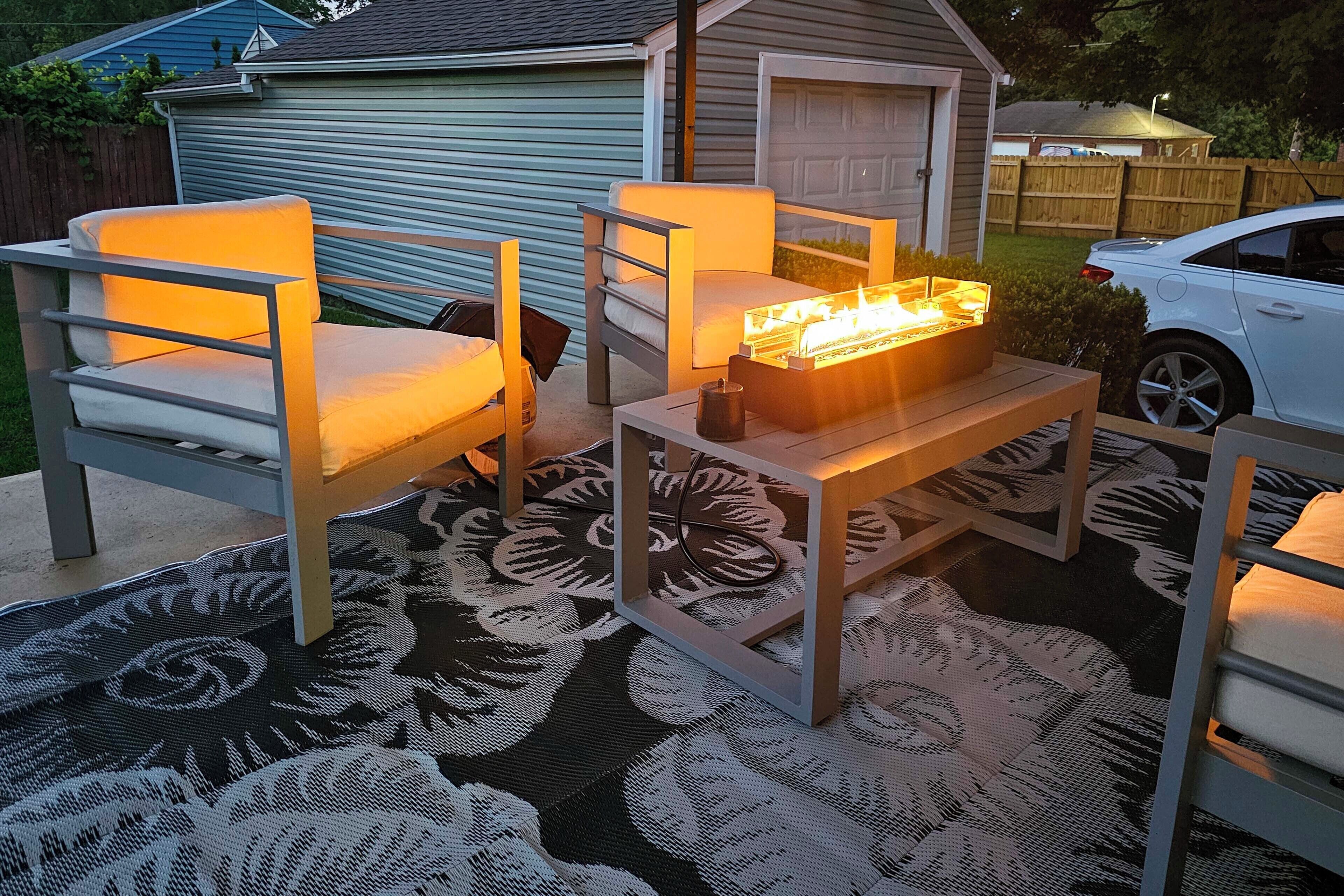 An outdoor seating area with two chairs and a table, a fire feature, and a patterned rug.