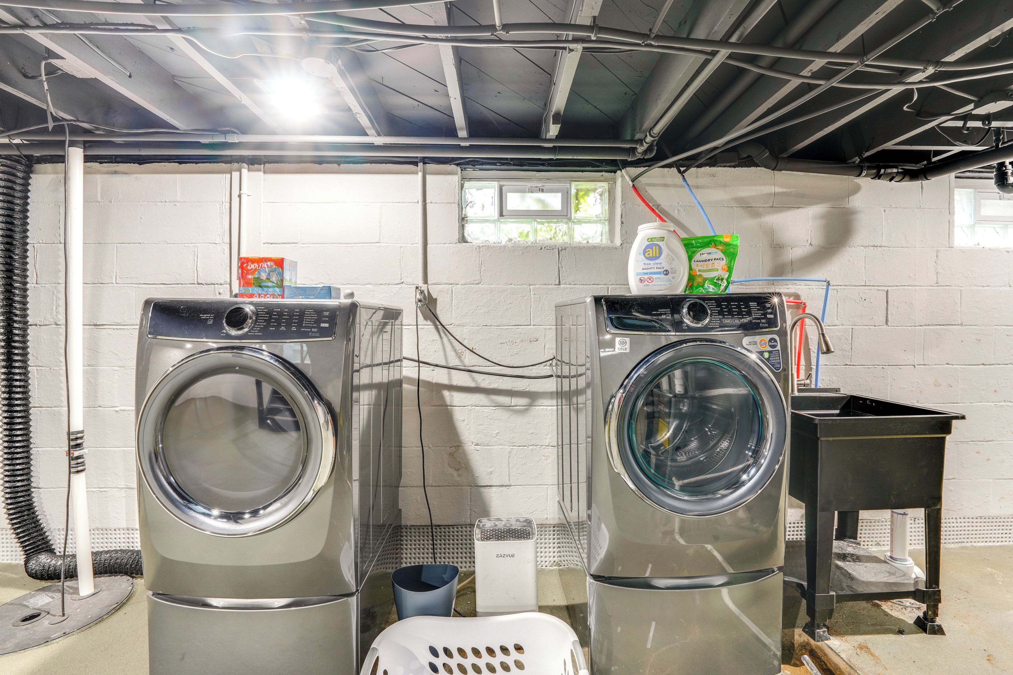 A laundry room with two front-loading washing machines, a small table, and a window with a view of greenery outside.