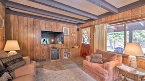 Ein gemütliches Wohnzimmer mit Holzwänden, einem Kamin, einem Fernseher und bequemen Sitzmöglichkeiten.