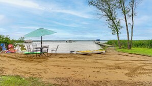 Uma praia arenosa com mesa e cadeiras, um caiaque e um canoa à beira-mar.
