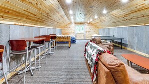 Um quarto aconchegante e bem iluminado, com paredes e teto de madeira, apresentando uma mesa comprida com cadeiras, um sofá e uma cama.