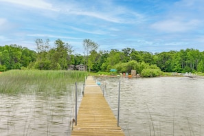 Een houten steiger die in het water uitloopt, omringd door weelderige begroeiing en een heldere lucht.