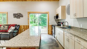 Uma cozinha moderna com bancada de granito, armários de madeira e vista para a floresta pela porta.