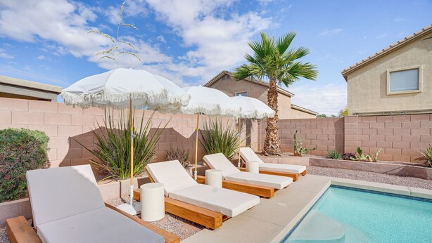 A poolside area with lounge chairs and umbrellas, a palm tree, and a brick wall. - 6 Mi to State Farm Stadium: Avondale Family Home! (Avondale)