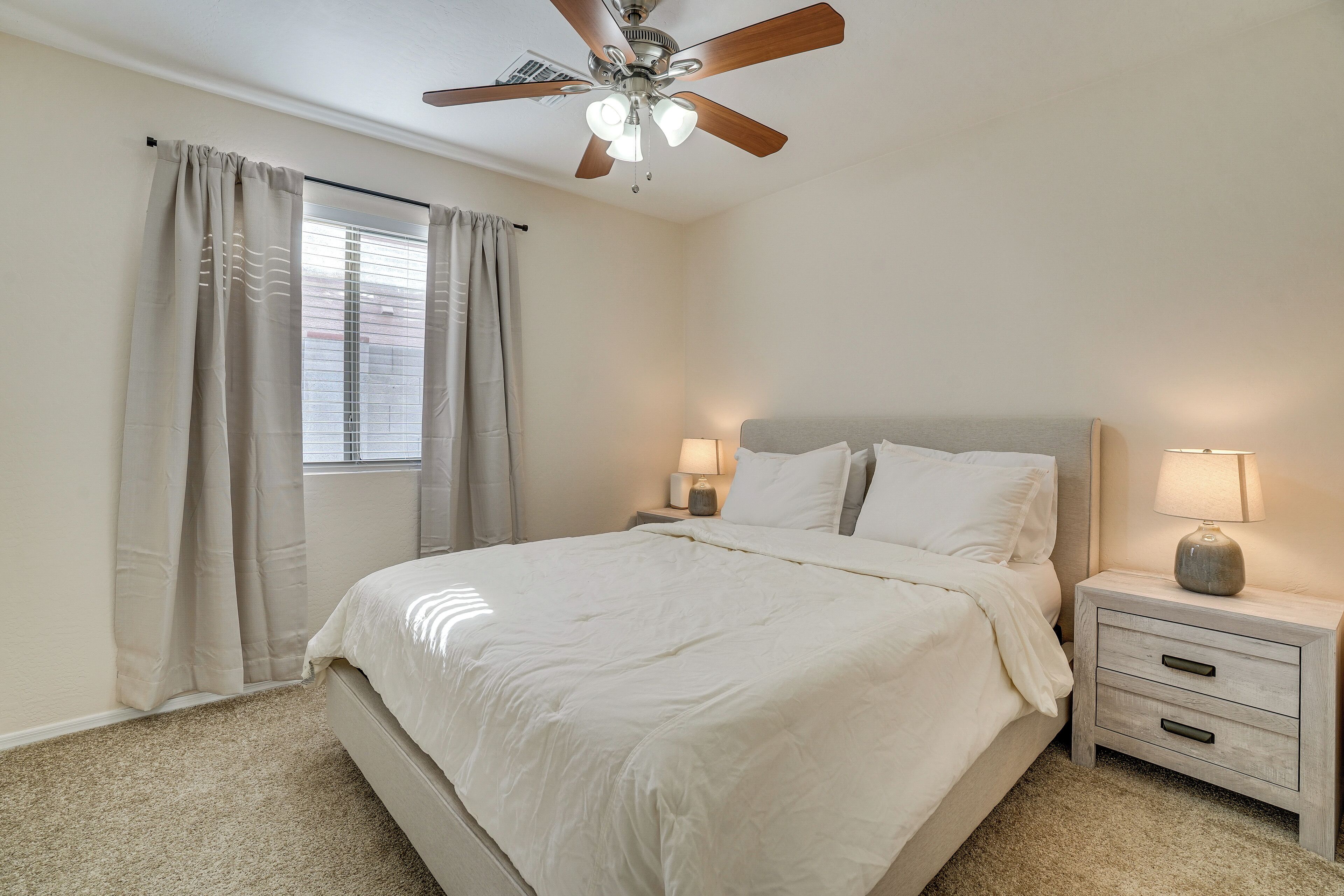 A bedroom with a bed, nightstands, a ceiling fan, and a window with curtains.