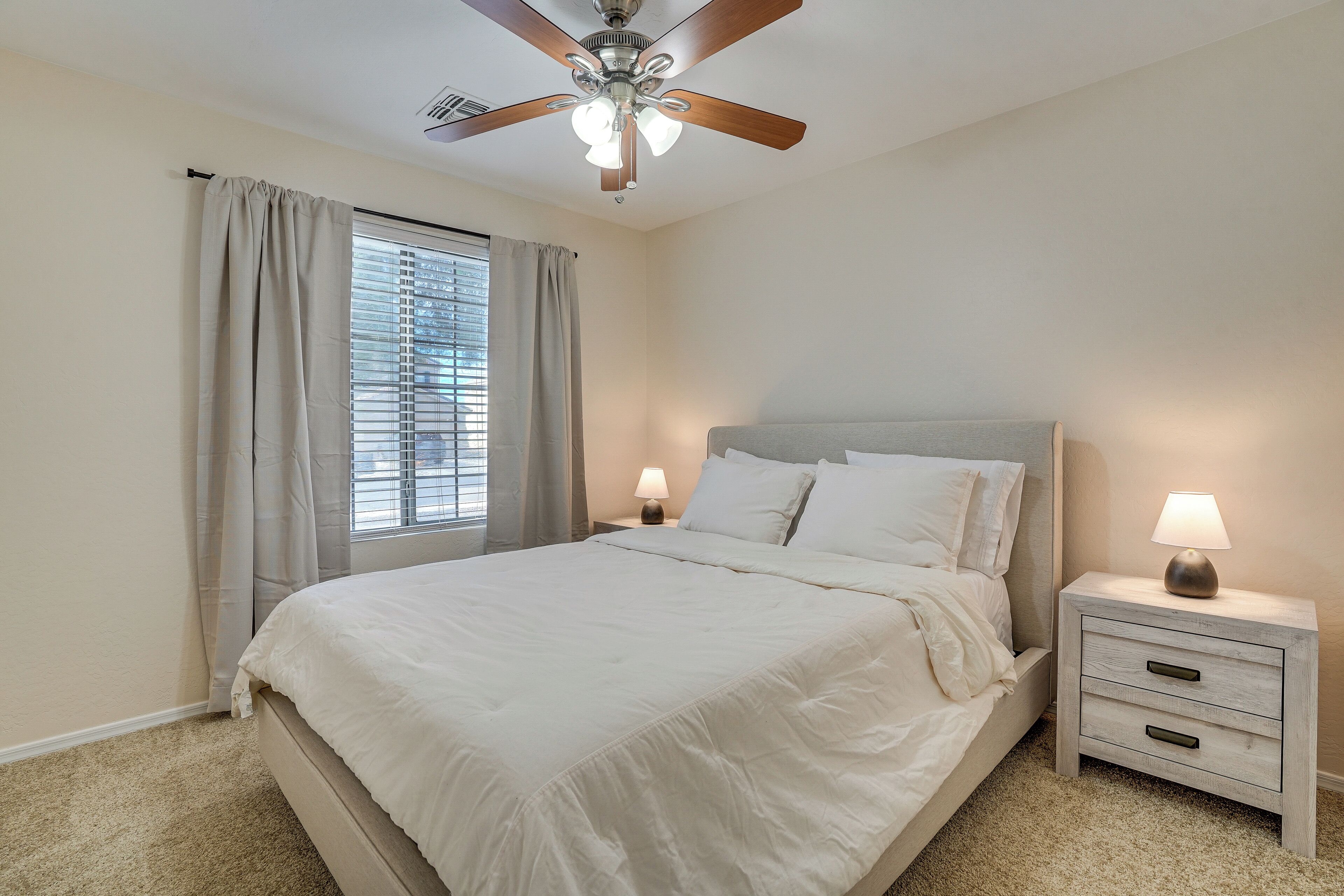 A bedroom with a bed, nightstands, a ceiling fan, and a window with curtains.
