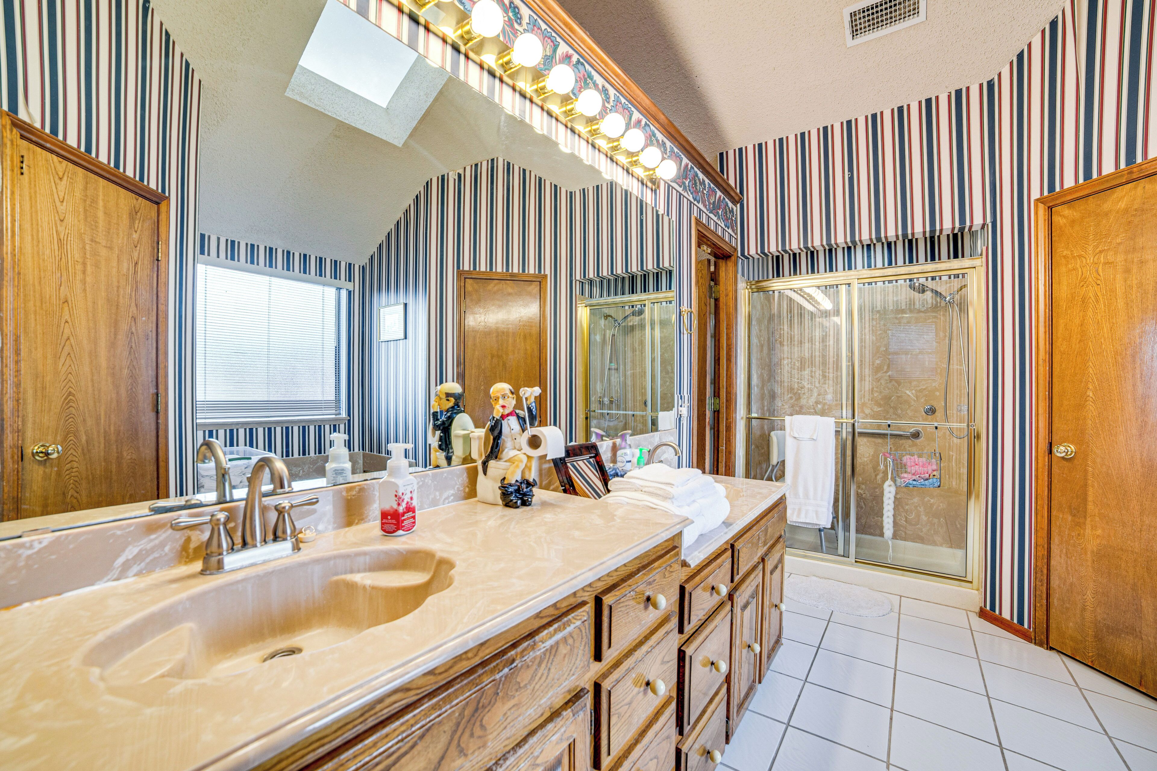A bathroom with a large vanity, a glass shower enclosure, and striped wallpaper.