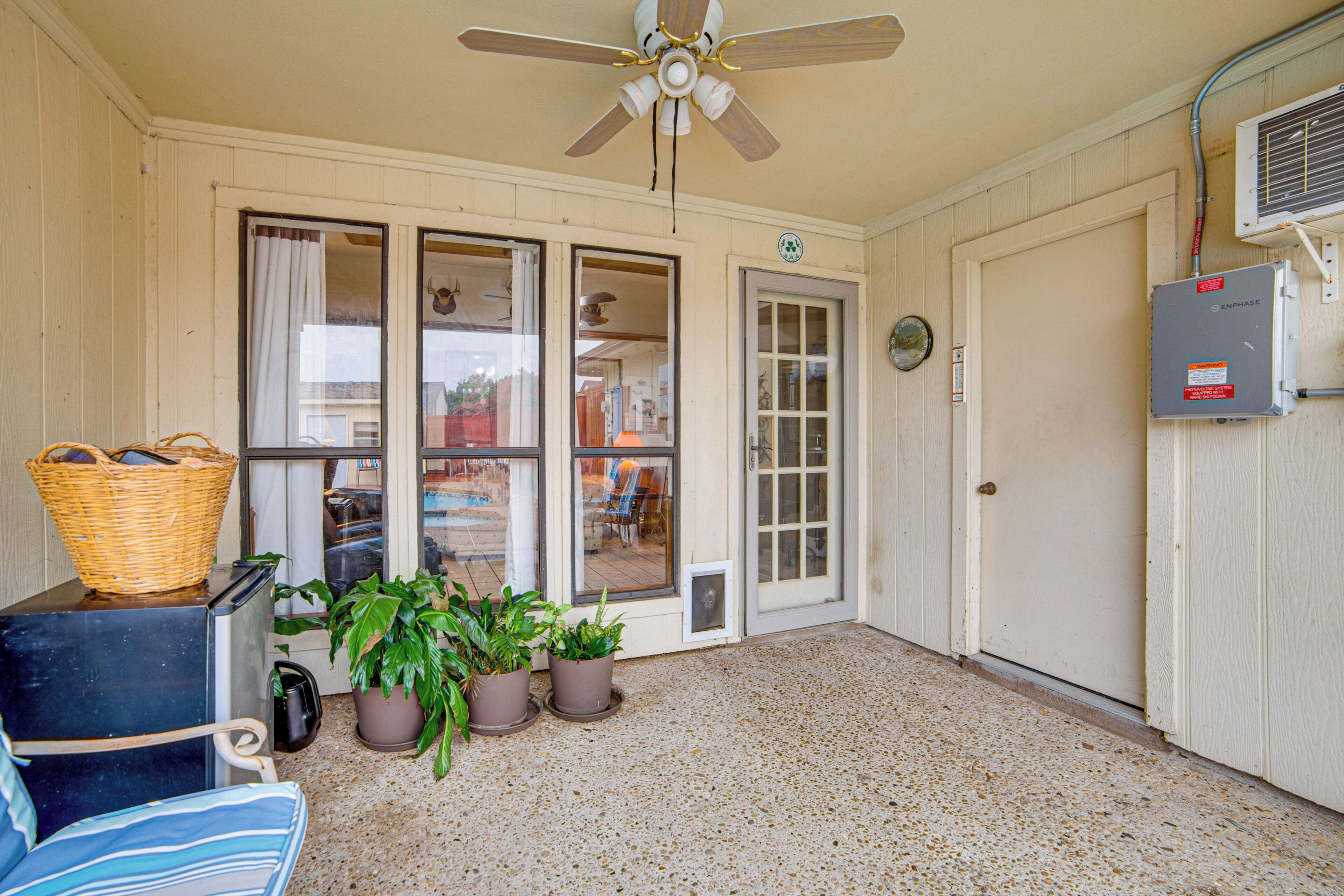 A room with a ceiling fan, a door, a window, a wall-mounted air conditioner, and a floor with a speckled pattern.