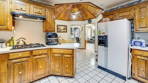 Une cuisine avec des meubles en bois, une cuisinière à gaz, un réfrigérateur et un ventilateur de plafond.