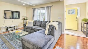 A modern living room with a sectional sofa, a flat-screen TV, and a glass coffee table. - Sunny Oakland Retreat w/ Patio & Cute Garden! (Oakland)