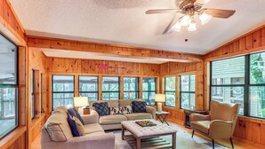A cozy living room with wooden walls, large windows, a ceiling fan, and a sectional sofa. - Cartecay River Retreat w/ Yard & Screened Porch! (Ellijay)