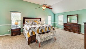 A bedroom with a bed, a nightstand, a dresser, a bench, and a ceiling fan.