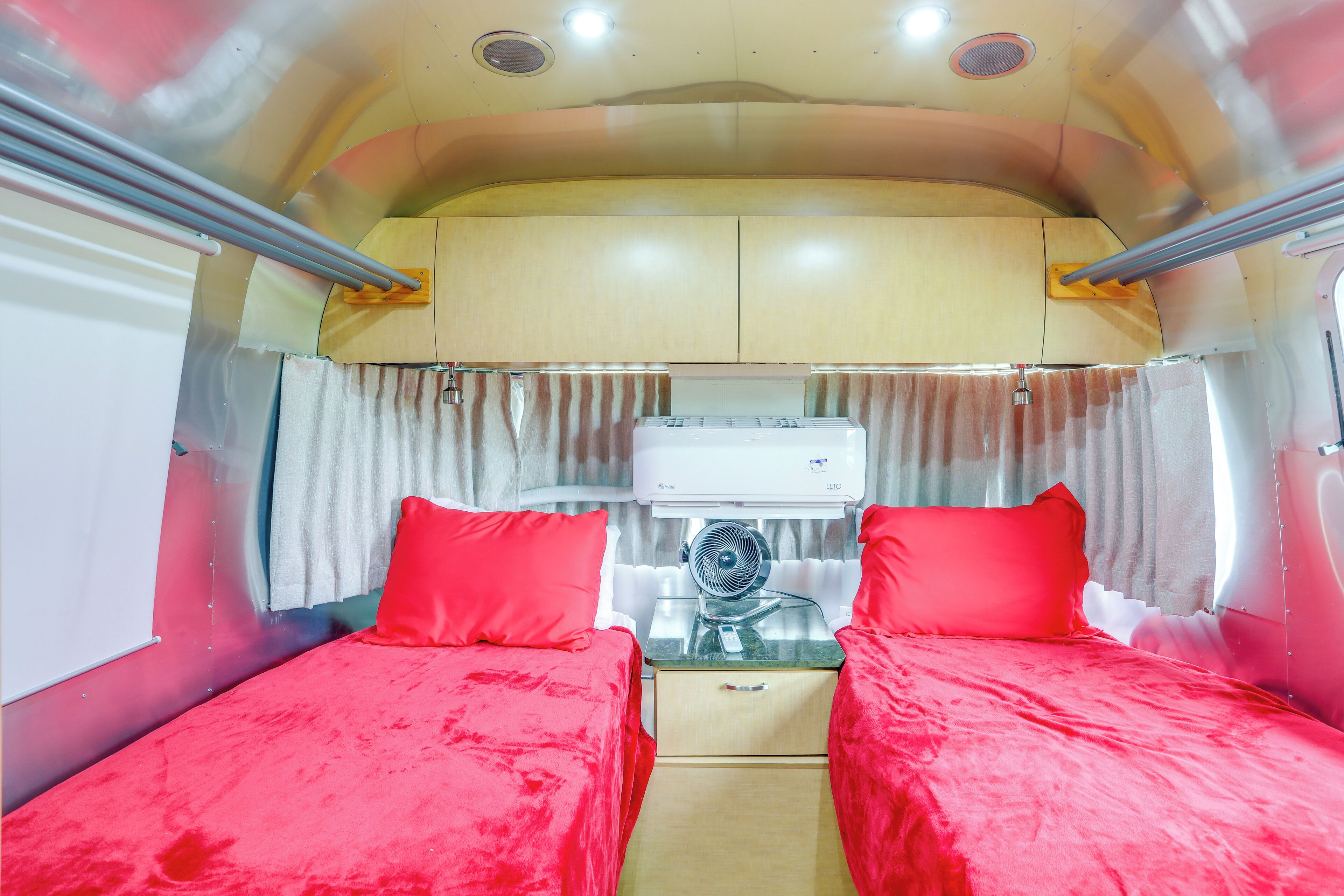 A compact, well-lit room with two beds, a small table, and a ceiling fan.