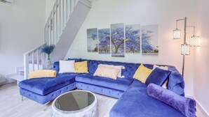 A modern living room with a blue sectional sofa, a glass coffee table, and a staircase. - River Access & Private Deck: Mountain View Retreat (Mountain View)