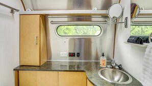 A compact kitchenette with a stainless steel sink, wooden cabinets, a window with a view, and a mirror. - River Access & Private Deck: Mountain View Retreat (Mountain View)