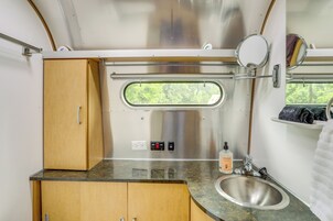 Una kitchenette compacta con un lavamanos de acero inoxidable, armarios de madera, un ventanal con vistas y un espejo.