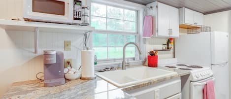 A kitchen with white cabinets, a granite countertop, a microwave, a coffee maker, a sink, a stove, and a refrigerator.