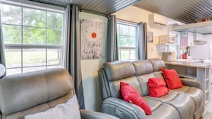 A cozy living area with a sofa and armchairs, a kitchen area with a microwave and sink, and large windows offering a view of greenery. - Swim On-site: Riverfront Studio in Mountain View! (Mountain View)