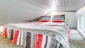 A bedroom with a sloped ceiling, a bed with striped bedding, and a window on the right. - Swim On-site: Riverfront Studio in Mountain View! (Mountain View)