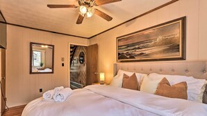 Quarto de hotel com uma cama grande, um ventilador de teto, um quadro, um espelho e uma porta.