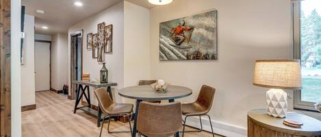 A dining area with a round table, four chairs, a lamp, and a painting on the wall.