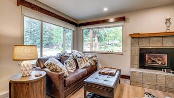 Ein Wohnzimmer mit Kamin, großen Fenstern, einer Couch, einem Couchtisch und einer Lampe.