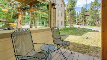 Een overdekt terras met twee metalen stoelen en een kleine tafel, uitkijkend op een woonstraat met huizen en bomen.
