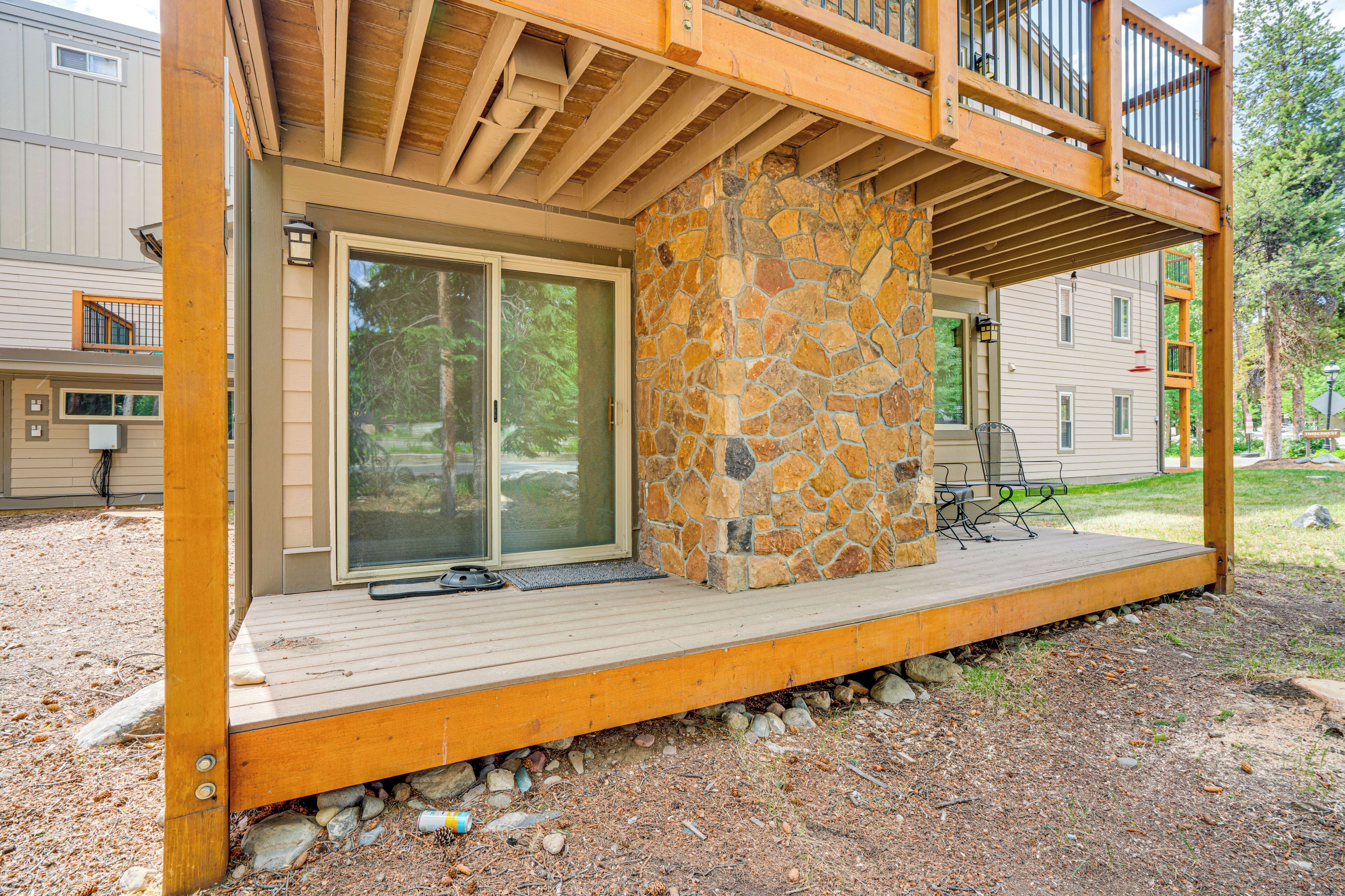 A covered outdoor area with a stone pillar, wooden deck, and a sliding glass door leading to a covered patio.