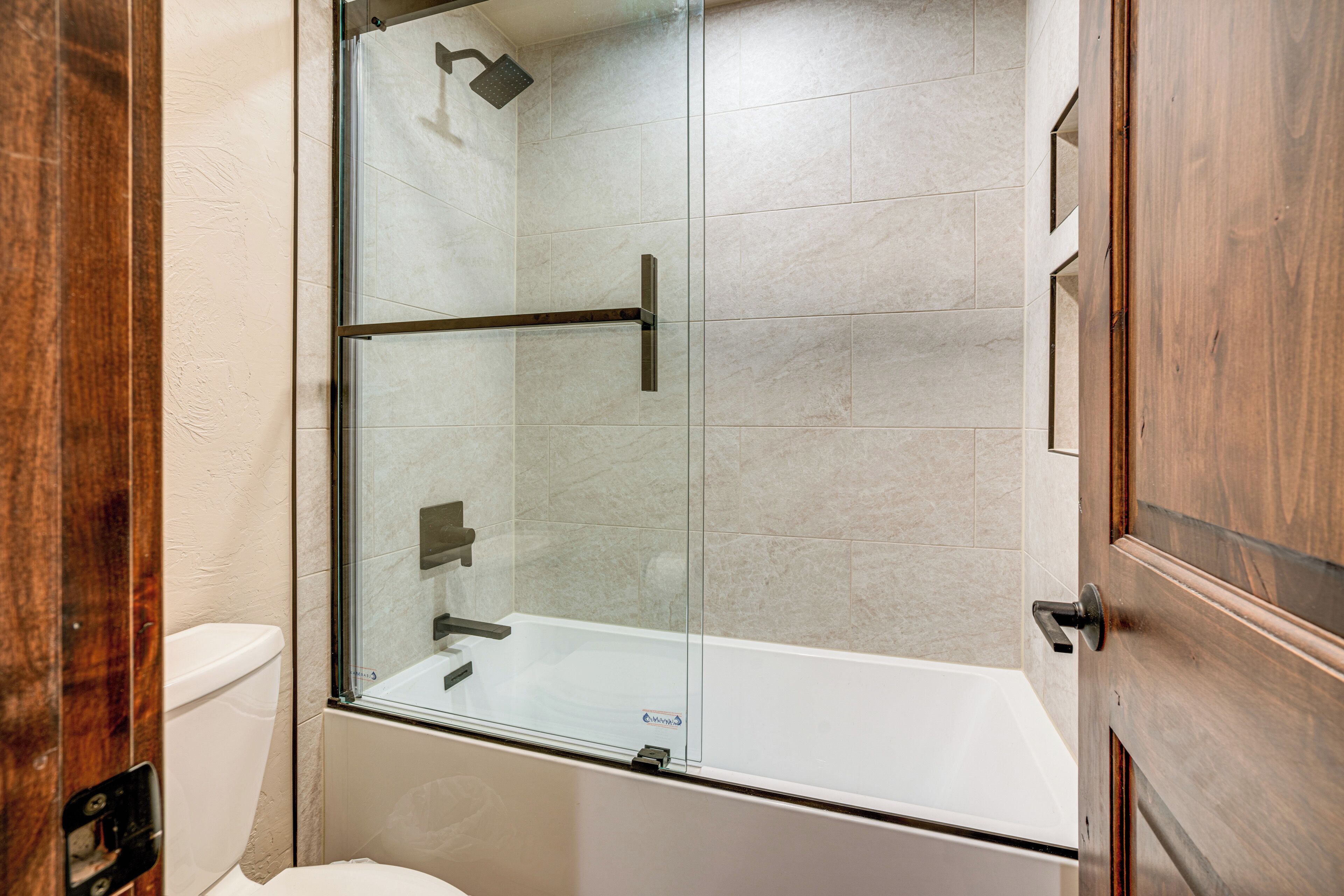Un baño moderno con ducha acristalada, inodoro blanco y puerta de madera.