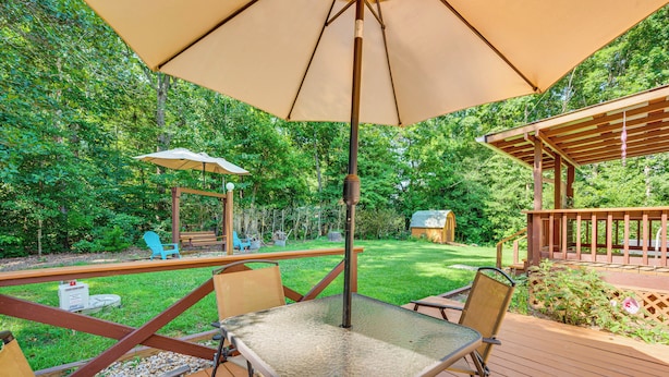 A patio with a table and chairs, surrounded by a wooden deck and a lush green garden. - 5 Min Walk to Badin Lake: 3BD Home w/ Deck & BBQ (New London)