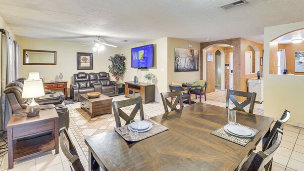 A spacious living room with a wooden dining table, comfortable seating, a television, and a kitchen area visible through an archway. - 4 Mi to Old Town: Pet-friendly Home w/ Fenced Yard (Albuquerque)