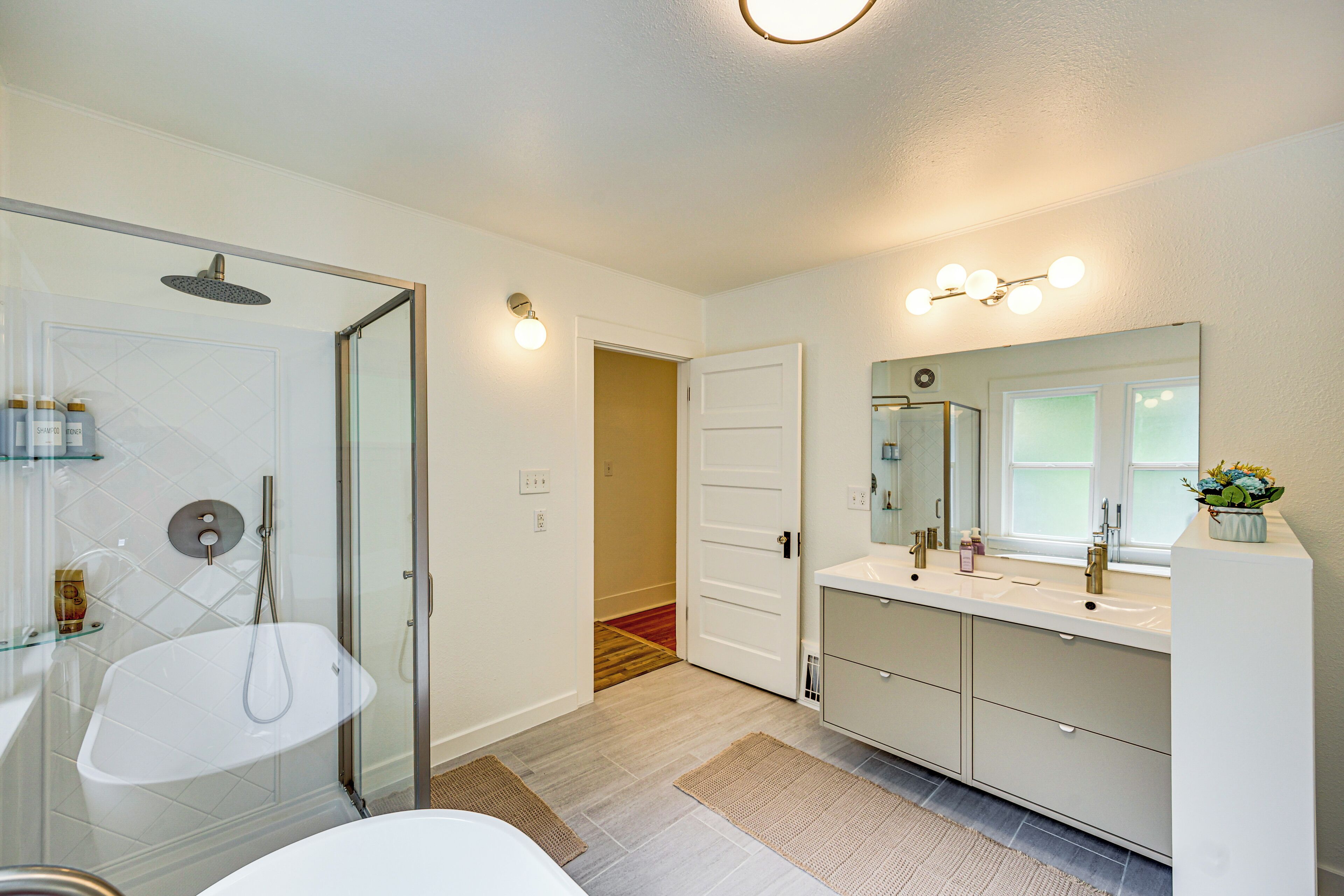 A modern bathroom with a glass-enclosed shower, a white sink, and a vanity with a large mirror.