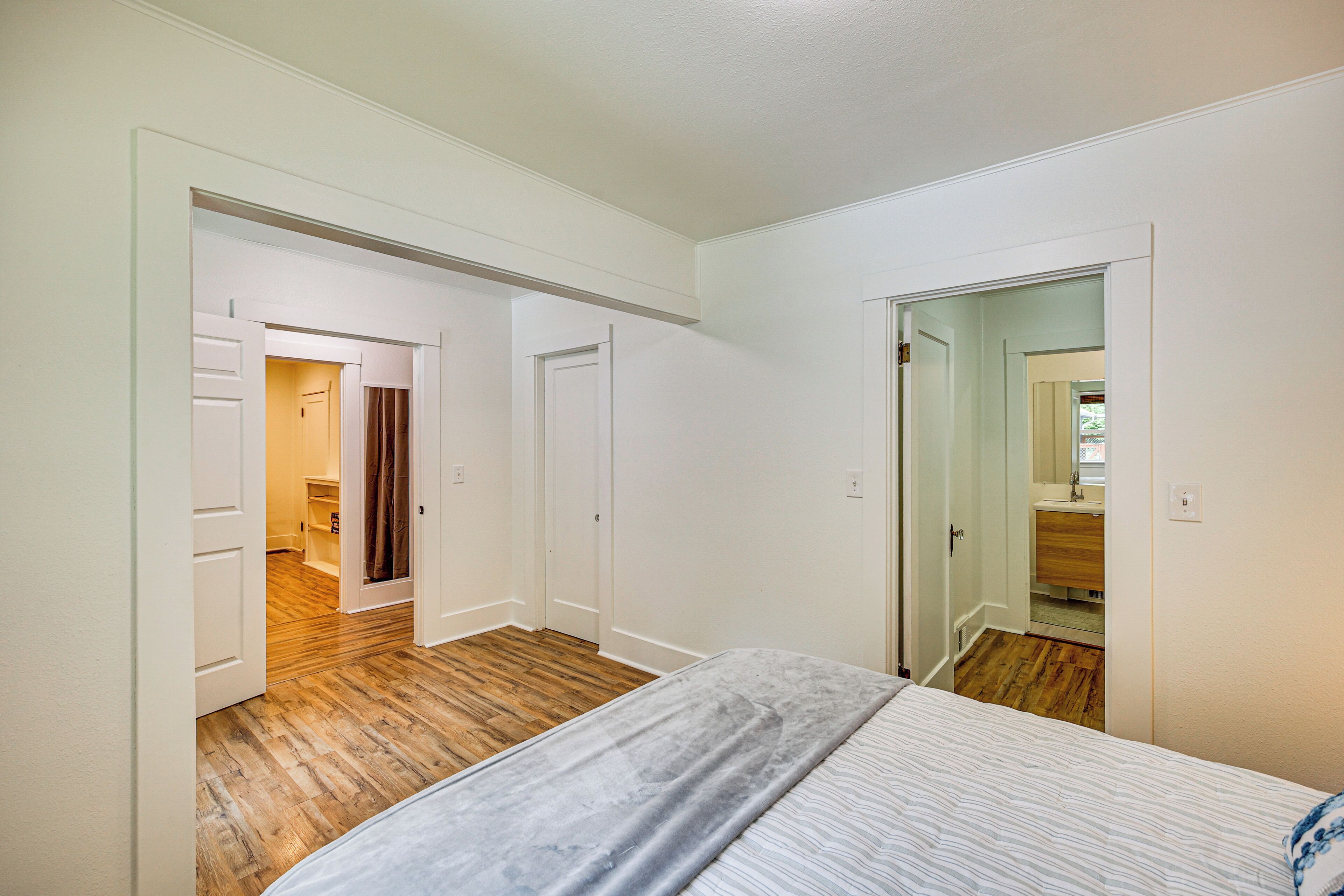 Un dormitorio con cama, suelo de madera, paredes blancas y una puerta que da a un baño.