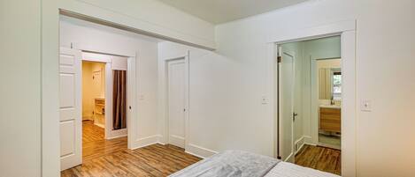 Un dormitorio con cama, suelo de madera, paredes blancas y una puerta que da a un baño.