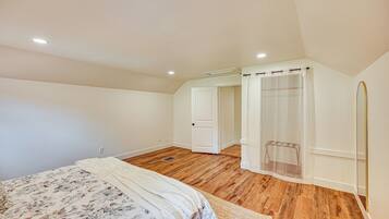 A bedroom with a wooden floor, a bed with a floral bedspread, a white door, and a shower area with a curtain.