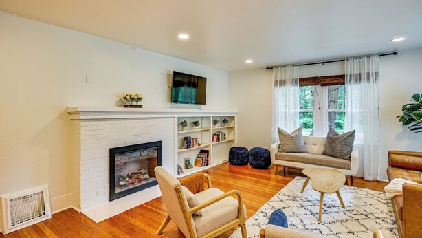 A living room with a fireplace, a sofa, a coffee table, and a bookshelf. - 7 Mi to Mt Rainier NP: Home w/ Private Hot Tub! (Ashford)