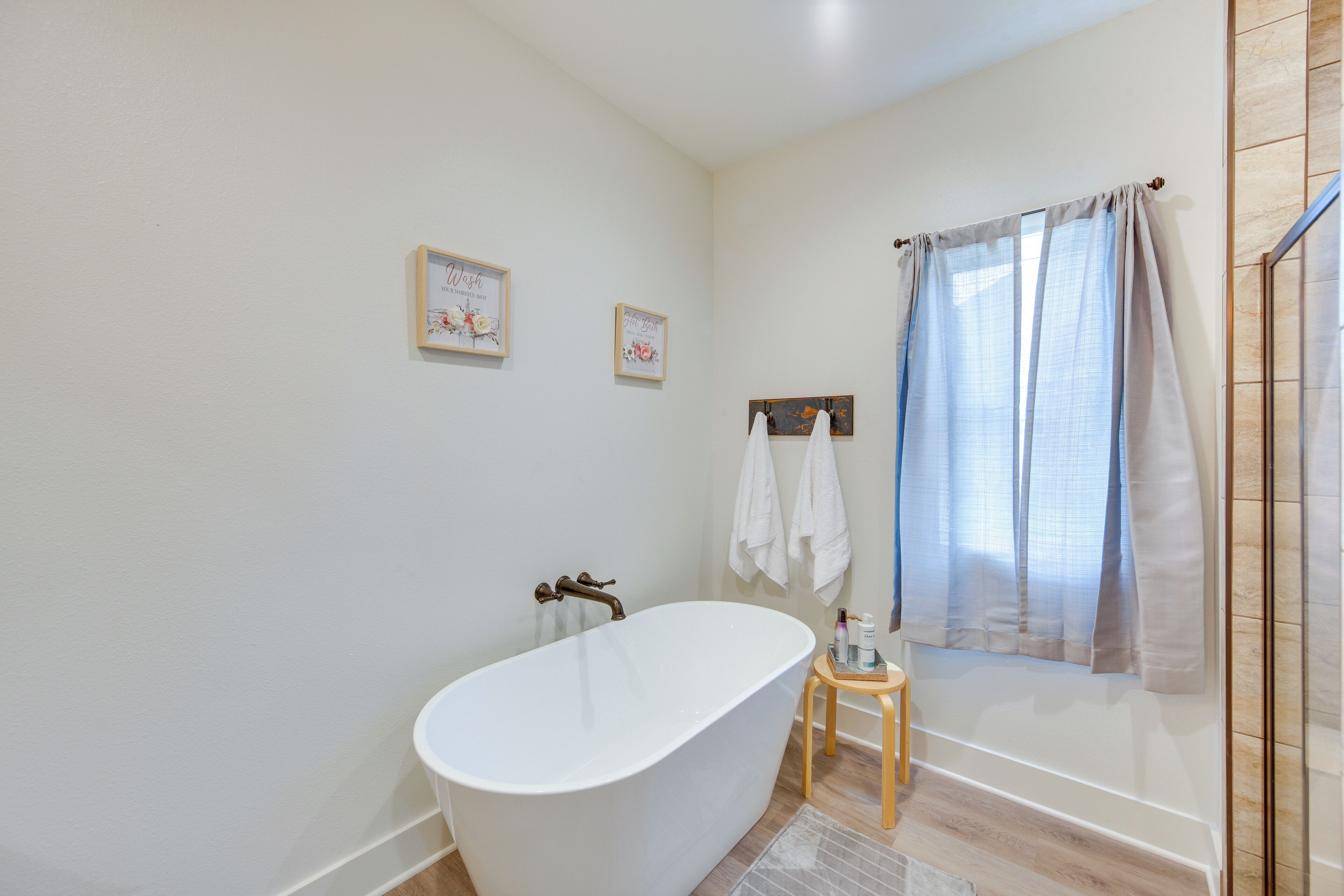 Een moderne badkamer met een vrijstaand bad, houten vloer en een klein houten krukje.