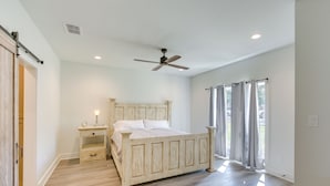 A bedroom with a bed, a nightstand, a ceiling fan, and a window with curtains. - Lake Palestine Vacation Rental - Steps to Water! (Frankston)
