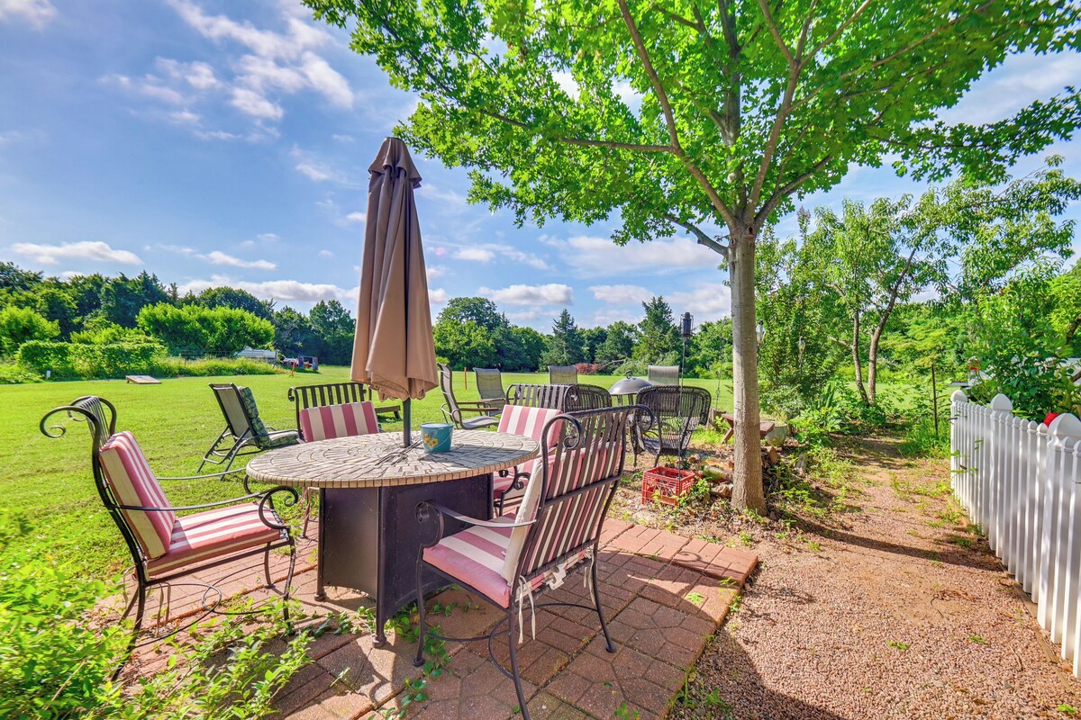 Une terrasse extérieure avec une table ronde et des chaises, entourée d’une clôture blanche en bois et d’une végétation luxuriante.