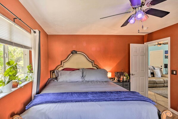 A bedroom with a bed, a ceiling fan, a window with plants, and a door leading to another room. - Updated Fort Myers Escape w/ Screened Lanai! (Fort Myers)