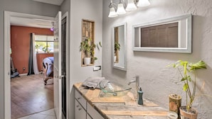 Une salle de bain avec un meuble-lavabo en bois, un vasque en verre et un miroir. On y trouve des plantes en pot et une serviette posée sur le comptoir.