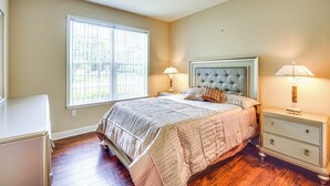 A bedroom with a large window, a bed with a tufted headboard, two bedside tables with lamps, and a dresser. - Family Home < 10 Mi to Flagler Beach: WFH Ready! (Palm Coast)