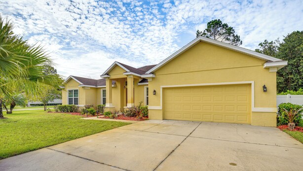 A two-story residential building with a yellow facade, a garage, and a well-maintained lawn. - Family Home < 10 Mi to Flagler Beach: WFH Ready! (Palm Coast)